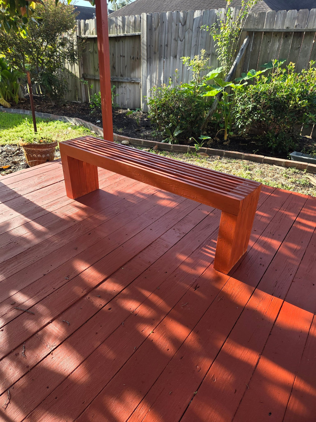 Red-stained slatted wooden bench on a matching red deck
