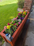 Raised planter box in red stain planted with colorful flowers