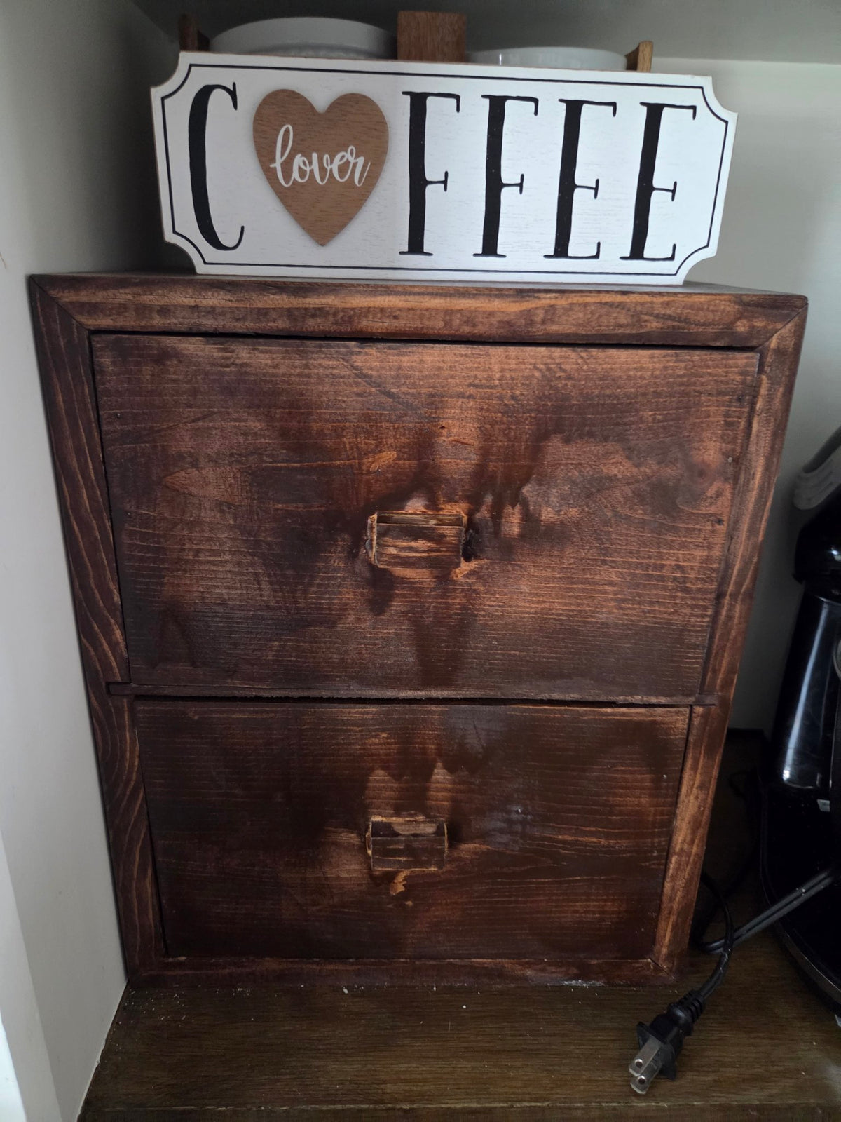 Small dark-stained wooden two-drawer cabinet used as a coffee station